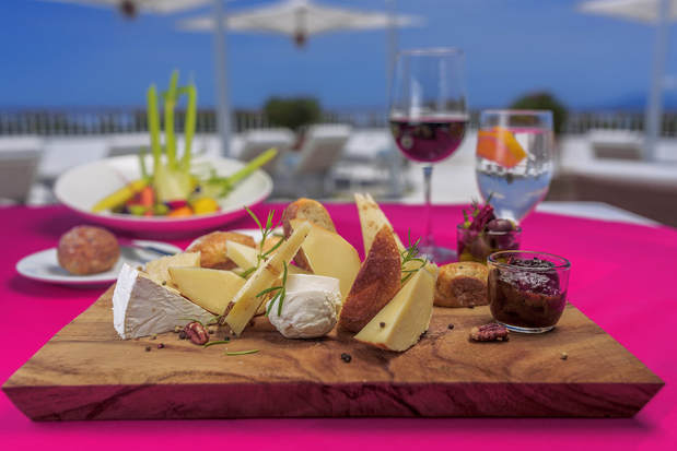 A cheese plate surrounded by cocktails, overlooking the pool